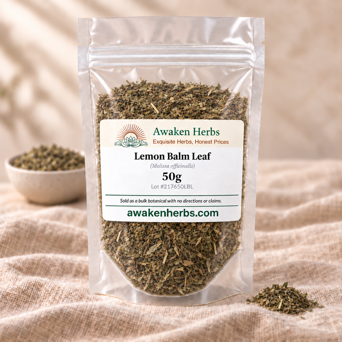 Awaken Herbs Lemon Balm Leaf 50g in a clear stand-up pouch on beige linen, with a softly blurred bowl and a small matching herb cluster.