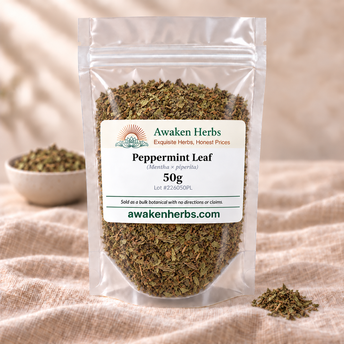 Awaken Herbs Peppermint Leaf 50g pouch on beige linen with matching dried herb in a blurred bowl and foreground cluster